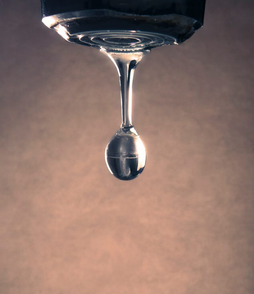 A water drop forms from a faucet.